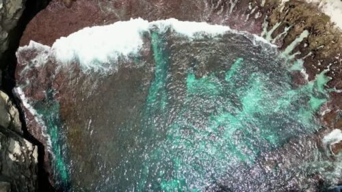 Video - Aerial drone view of Broken Beach in Nusa Penida, Bali, Indonesia. Powerful ocean waves crash against the circular limestone cove, revealing turquoise water patterns over rocky reef formations