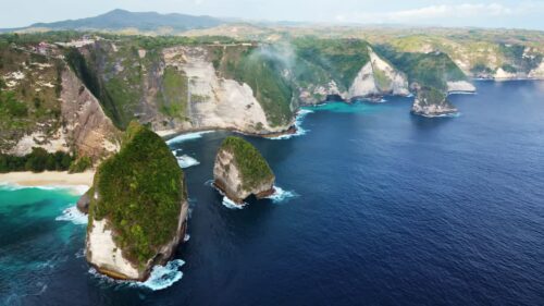 Video - Aerial drone view of Kelingking Beach in Nusa Penida, Bali. Massive limestone cliffs and offshore rock formations rise from deep blue ocean waters