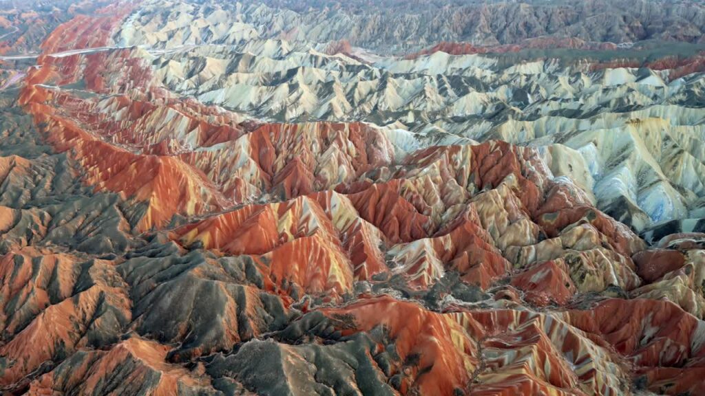 Video - Aerial drone view of the colorful Zhangye Danxia Landform Geological Park in Zhangye, Gansu Province, China. Dramatic layered sandstone mountains display vibrant red, orange, and pastel mineral stripes across rolling desert hills