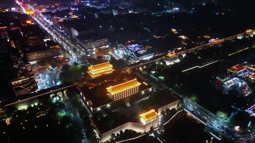 Video - Aerial drone view of the illuminated Xi'an City Wall and Yongning Gate. Traditional Chinese architecture glows in warm golden light, surrounded by busy city streets and modern urban development