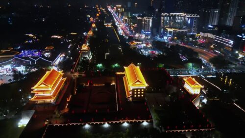 Video - Aerial drone view of the illuminated Xi'an City Wall and Yongning Gate. Traditional Chinese architecture glows in warm golden light, surrounded by busy city streets and modern urban development