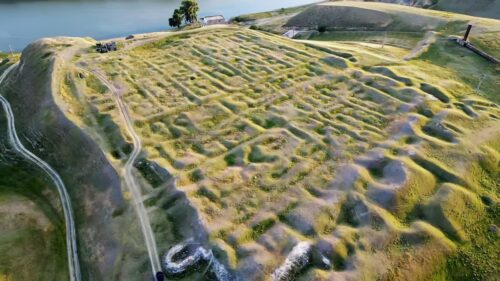 Video - Aerial drone view of the Danube River flowing through the Iron Gates Gorge along the Romania Serbia border. The wide river curves around a forested island, surrounded by agricultural fields and rolling hills