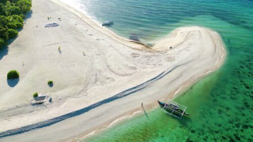 Video - Aerial drone view of the pristine white sandbar of Ditaytayan Island in Culion, Palawan, Philippines. Turquoise shallow waters surround the curved sandbank with crystal-clear coral reefs visible beneath the surface