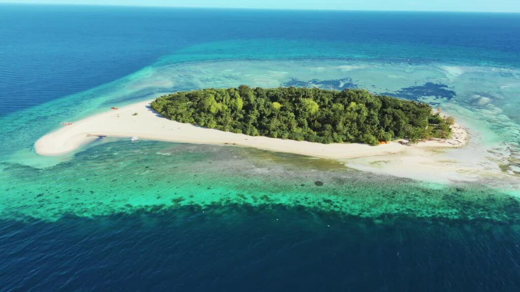 Video - Aerial drone view of a small tropical island surrounded by turquoise ocean and coral reefs in the Philippines. White sand beaches and dense green vegetation create a pristine island paradise
