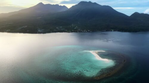 Video - Aerial drone view of a curved sandbar in Coron Bay, Palawan, Philippines, surrounded by calm turquoise waters with dramatic mountain silhouettes in the background
