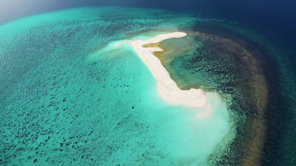 Video - Aerial drone view of a curved sandbar in Coron Bay, Palawan, Philippines, surrounded by calm turquoise waters with dramatic mountain silhouettes in the background