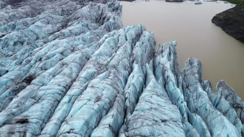 Video - Aerial drone view of deep crevasses of Falljokull glacier, an outlet of Vatnajokull in South Iceland. Dramatic blue ice ridges and dark volcanic ash streaks create powerful Arctic landscape scenery under cloudy sky