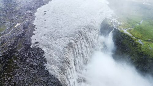 Video - Aerial drone view of Dettifoss waterfall plunging into Jokulsargljufur canyon in Northeast Iceland. Massive curtain of water spills over rugged basalt cliffs surrounded by barren Icelandic highlands