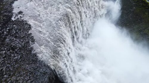 Video - Aerial drone view of Dettifoss waterfall plunging into Jokulsargljufur canyon in Northeast Iceland. Massive curtain of water spills over rugged basalt cliffs surrounded by barren Icelandic highlands