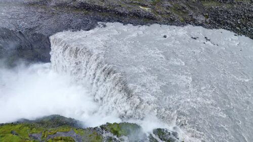 Video - Aerial drone view of Dettifoss waterfall plunging into Jokulsargljufur canyon in Northeast Iceland. Massive curtain of water spills over rugged basalt cliffs surrounded by barren Icelandic highlands