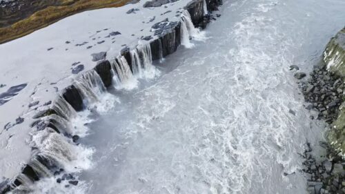 Video - Aerial drone view of Dettifoss waterfall cascading over dark volcanic cliffs. Heavy glacial currents crash into the canyon below