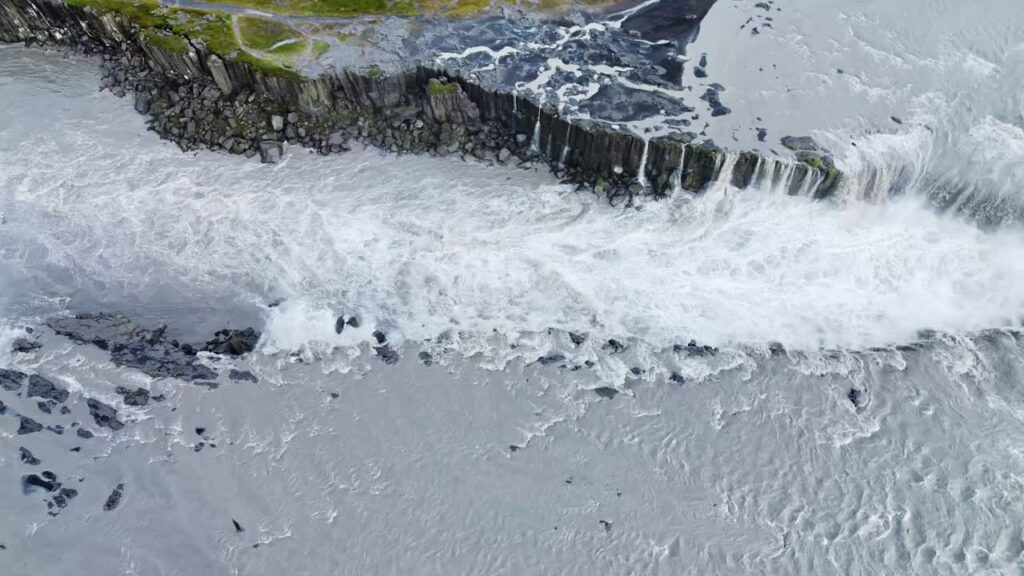 Video - Aerial drone view of Dettifoss waterfall plunging into Jokulsargljufur canyon in Northeast Iceland. Massive curtain of water spills over rugged basalt cliffs surrounded by barren Icelandic highlands