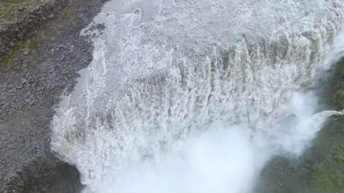 Video - Aerial drone view of crashing glacial water hitting the canyon floor at Dettifoss. Thick spray and mist rise dramatically from the impact zone