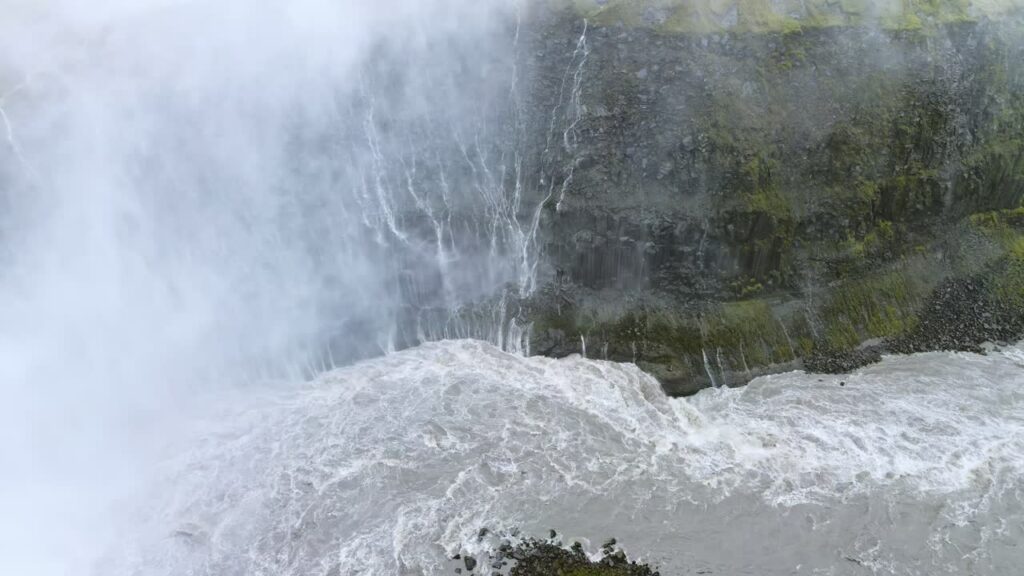 Video - Aerial drone view of Hafragilsfoss waterfall located downstream from Dettifoss. Powerful whitewater flows through a steep volcanic canyon surrounded by layered basalt rock formations