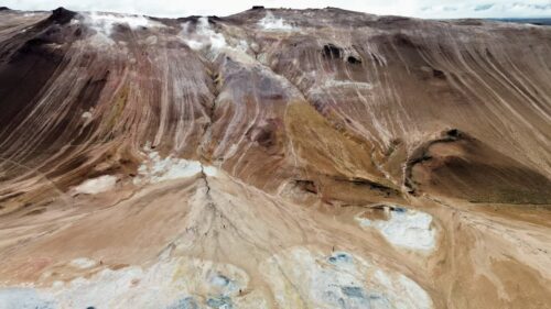 Video - Aerial drone view of the colorful rhyolite slopes of Namafjall. Steam vents rise from mineral streaked hills in shades of brown, red, and ochre, highlighting Iceland's active geothermal forces