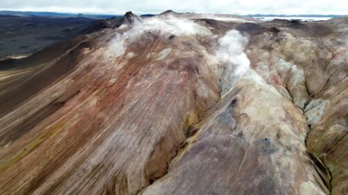Video - Aerial drone view of the colorful rhyolite slopes of Namafjall. Steam vents rise from mineral streaked hills in shades of brown, red, and ochre, highlighting Iceland's active geothermal forces