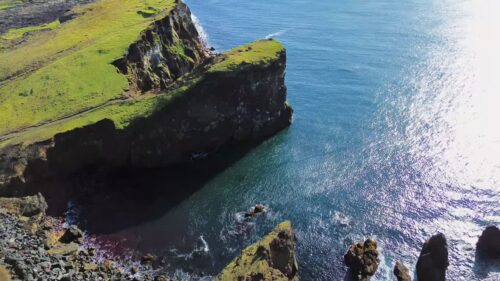 Video - Aerial drone view of dramatic sea cliffs rising above the North Atlantic Ocean. Steep volcanic rock formations drop into deep blue water along Iceland's rugged coastline