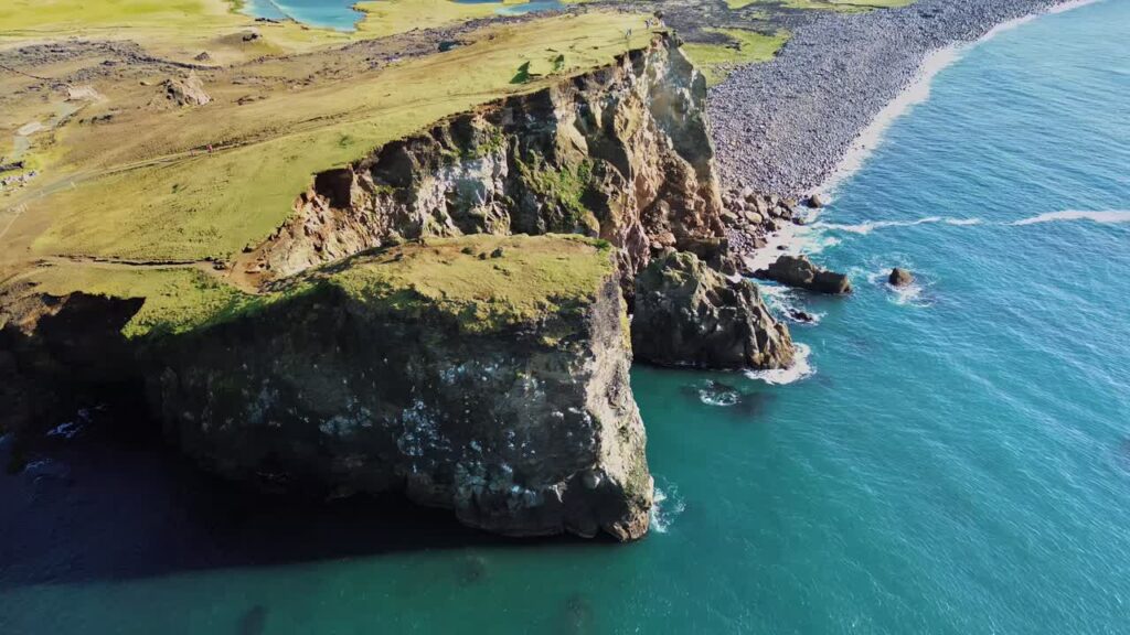 Video - Aerial drone view of dramatic sea cliffs rising above the North Atlantic Ocean. Steep volcanic rock formations drop into deep blue water along Iceland's rugged coastline