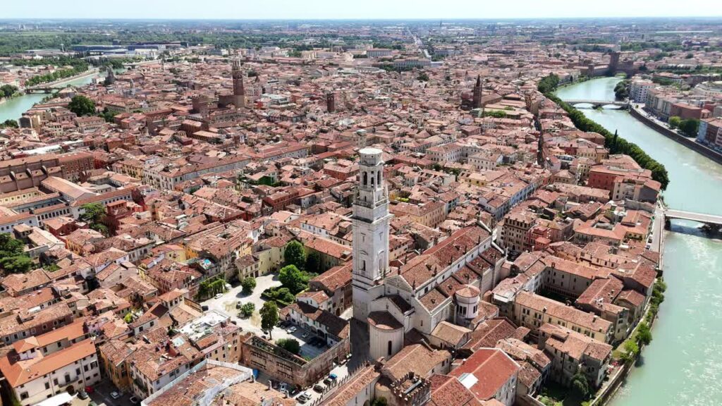 Video - Aerial drone view of Verona's historic city center surrounded by the curved Adige River. The Verona Cathedral bell tower rises above red rooftops and historic architecture