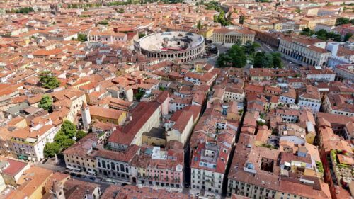Video - Aerial drone view of the historic center of Verona toward the ancient Roman Arena amphitheater surrounded by colorful buildings and city streets