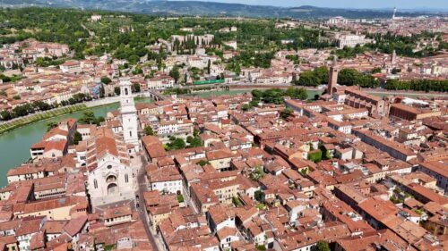 Video - Aerial drone view of Verona's medieval cityscape featuring Verona Cathedral and historic rooftops with the Adige River flowing through the city