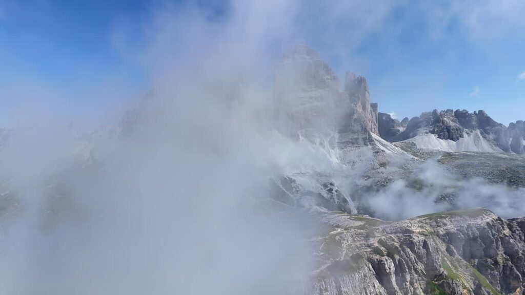 Video - Aerial drone view of the famous Tre Cime di Lavaredo with towering rock spires rising above alpine meadows and hiking trails in the Dolomites UNESCO World Heritage site