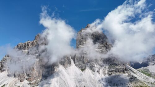 Video - Aerial drone view of the famous Tre Cime di Lavaredo with towering rock spires rising above alpine meadows and hiking trails in the Dolomites UNESCO World Heritage site