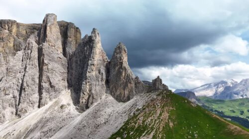 Video - Aerial drone view of dramatic limestone towers rising above alpine meadows in the Dolomites, Italy, under a cloudy mountain sky