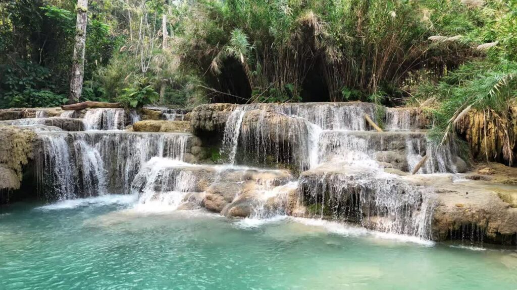 Video - Aerial drone view of tiered waterfalls at Kuang Si Falls near Luang Prabang, Laos with turquoise pools and flowing cascades surrounded by lush tropical jungle