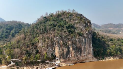 Video - Aerial drone view of water flowing over limestone rocks into a turquoise natural pool at Kuang Si Falls, one of the most famous waterfalls in Laos