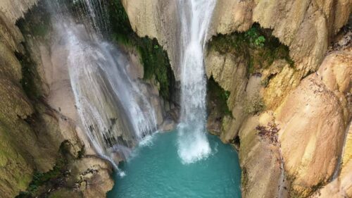 Video - Aerial drone view of multi-level turquoise pools and cascading waterfalls at Kuang Si Falls, surrounded by lush tropical forest in northern Laos