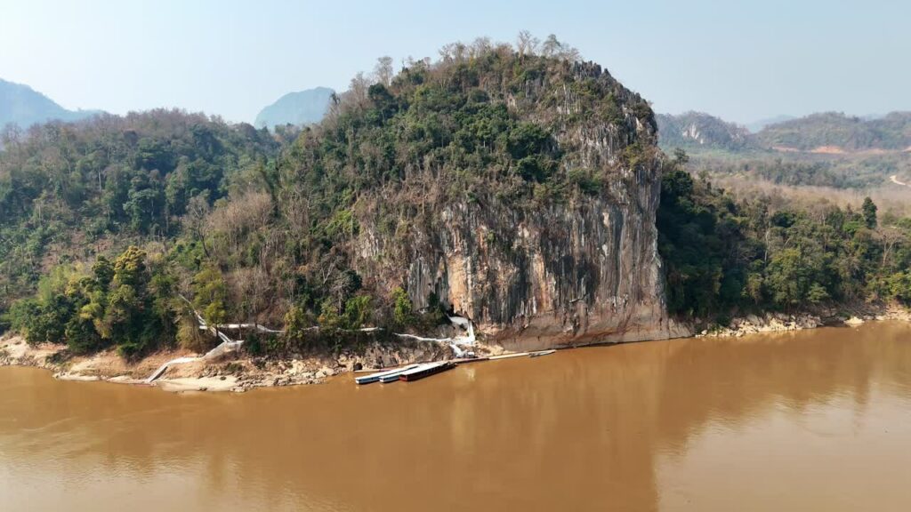 Video - Aerial drone view of water flowing over limestone rocks into a turquoise natural pool at Kuang Si Falls, one of the most famous waterfalls in Laos