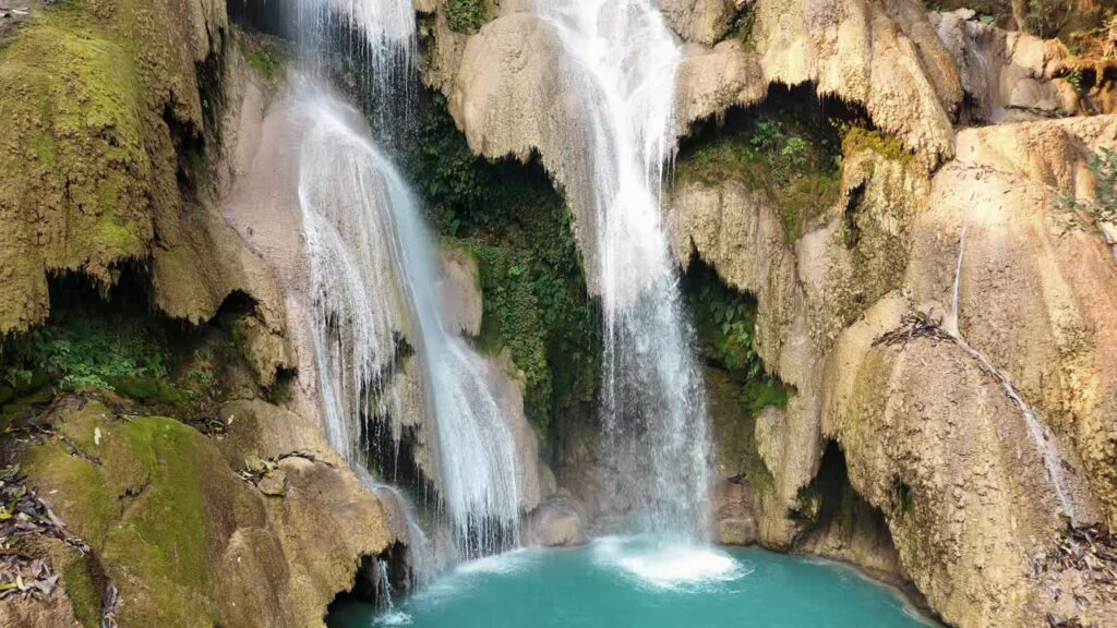 Video - Aerial drone view of multi-level turquoise pools and cascading waterfalls at Kuang Si Falls, surrounded by lush tropical forest in northern Laos