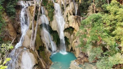Video - Aerial drone view of multi-level turquoise pools and cascading waterfalls at Kuang Si Falls, surrounded by lush tropical forest in northern Laos