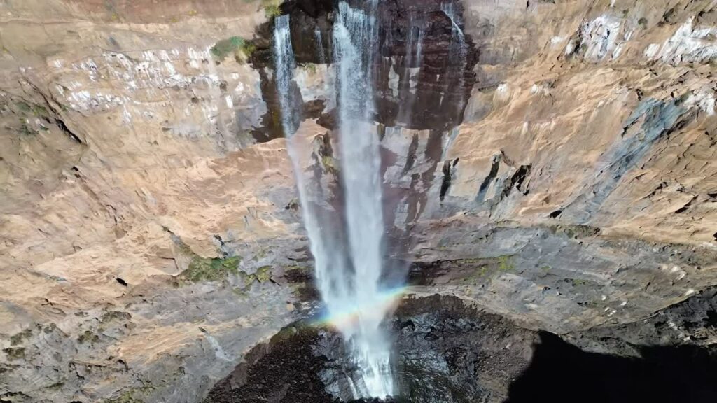 Video - Aerial drone view of Maletsunyane Falls in Lesotho, a powerful waterfall plunging down a high sandstone cliff with a rainbow forming in the mist below
