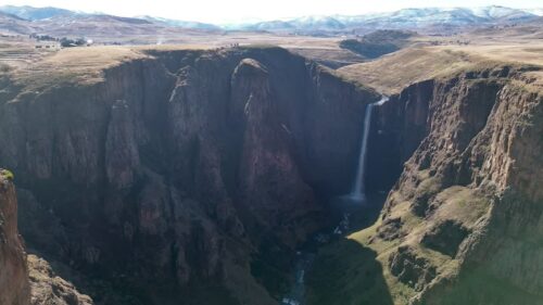 Video - Aerial drone view of Maletsunyane Falls dropping into a deep canyon in the Lesotho highlands, surrounded by rugged cliffs and vast mountain landscapes