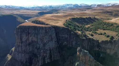 Video - Aerial drone view across dramatic canyon cliffs and mountain plateaus in the Lesotho highlands, showing the rugged terrain and remote African landscape