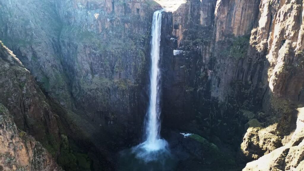 Video - Aerial drone view of Maletsunyane Falls dropping into a deep canyon in the Lesotho highlands, surrounded by rugged cliffs and vast mountain landscapes