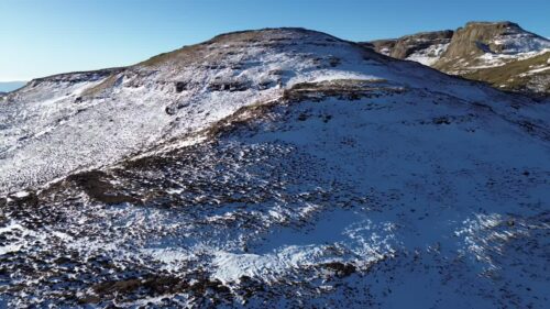 Video - Aerial drone view of snow covering mountain slopes in the Lesotho highlands, with rugged terrain and winter landscape under clear blue skies