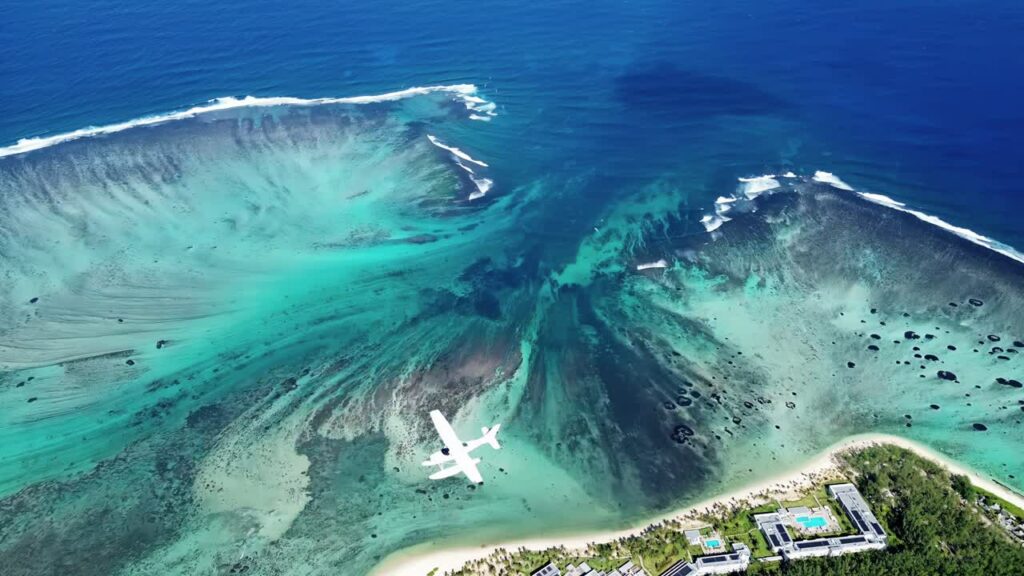Video - Aerial drone view of turquoise lagoon waters and coral reef formations in Mauritius, with waves breaking along the reef line in the Indian Ocean