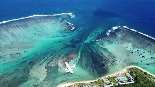 Video - Aerial drone view of turquoise lagoon waters and coral reef formations in Mauritius, with waves breaking along the reef line in the Indian Ocean