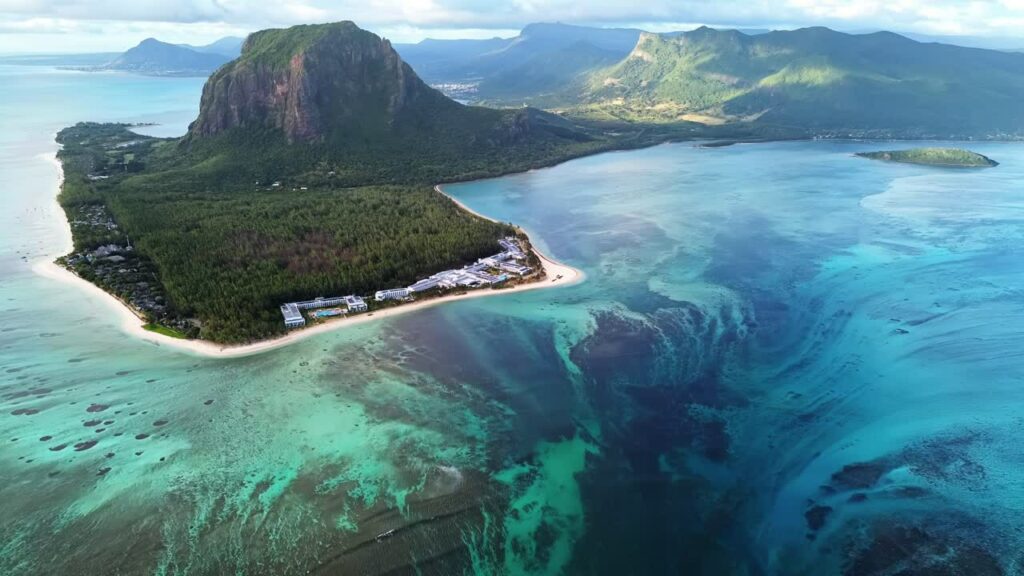 Video - Aerial drone view of Le Morne Brabant peninsula in Mauritius, showing coral reefs, turquoise lagoon waters, and the iconic mountain rising above the tropical coastline