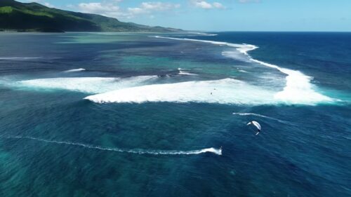 Video - Aerial drone view of kitesurfers riding waves near the coral reef barrier in Mauritius, with deep blue ocean on one side and shallow turquoise lagoon on the other