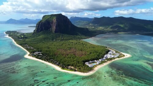 Video - Aerial drone view of Le Morne Brabant peninsula in Mauritius, showing coral reefs, turquoise lagoon waters, and the iconic mountain rising above the tropical coastline