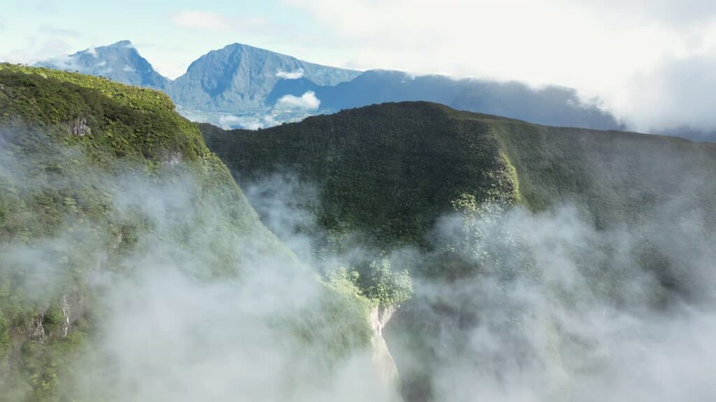 Video - Aerial drone view of rolling rainforest hills and mountain peaks emerging through drifting clouds, showcasing Madagascar's rugged tropical highland landscape