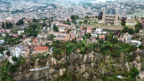 Video - Aerial drone view above Antananarivo with the city skyline spread across surrounding hills, showing dense urban neighborhoods and the large historic palace complex overlooking Madagascar's capital