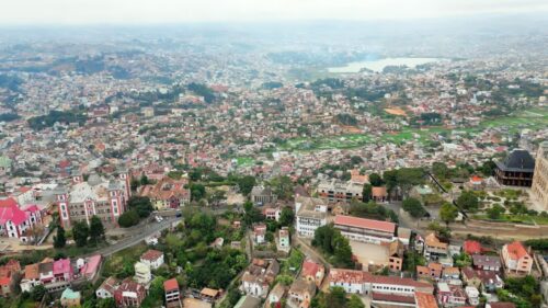 Video - Aerial drone view above Antananarivo with the city skyline spread across surrounding hills, showing dense urban neighborhoods and the large historic palace complex overlooking Madagascar's capital