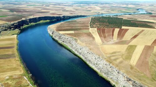 Video - Aerial drone view of the Tigris River winding through agricultural fields and cliffs in the Mesopotamia region of southeastern Turkey, showing fertile farmland and dramatic river landscapes