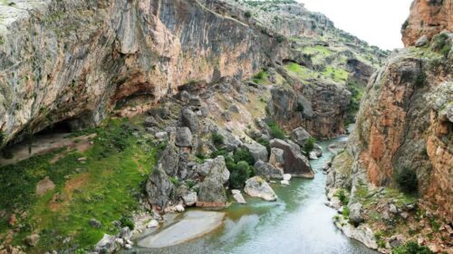 Video - Aerial drone view through a rocky canyon with steep cliffs and a flowing river below, capturing the rugged natural landscape of the historic Mesopotamia region