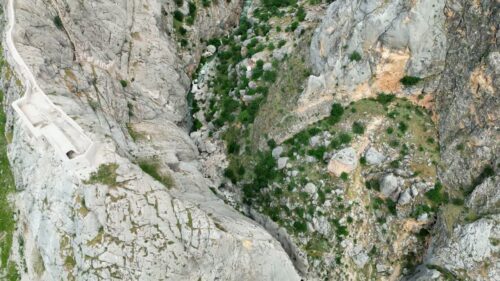 Video - Aerial drone view of a deep rocky gorge with scattered vegetation and a river running through the canyon floor in Mesopotamia